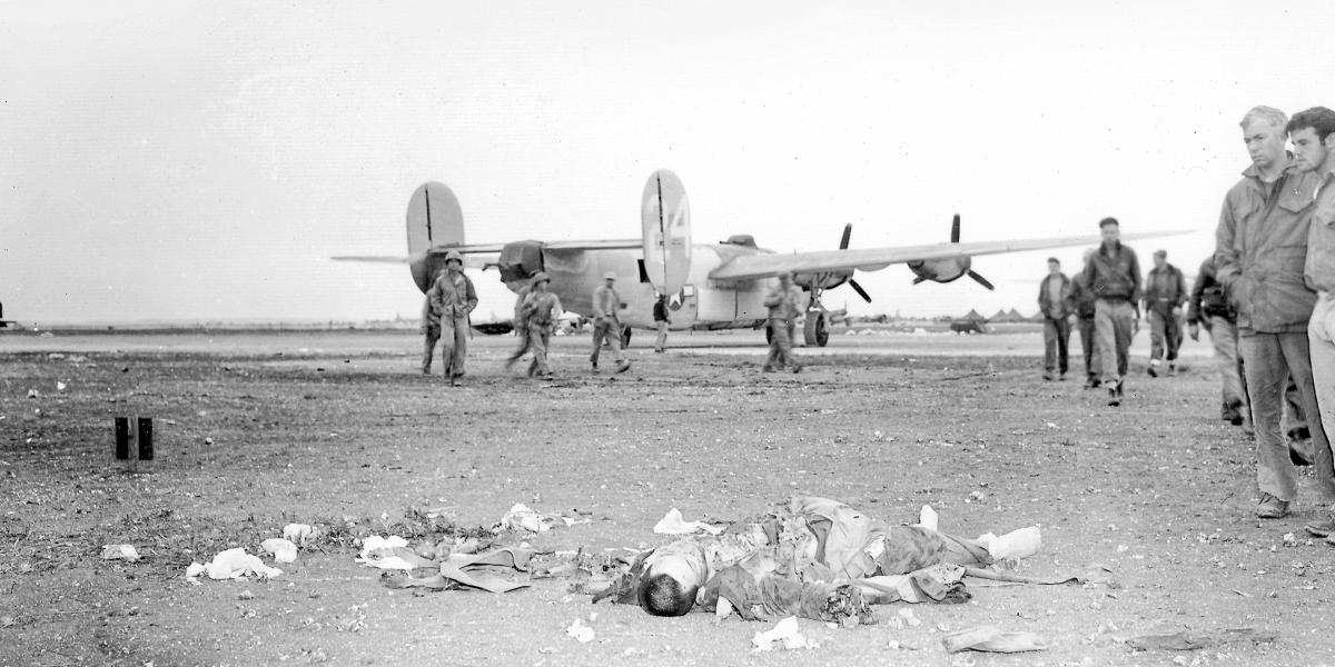 Marines at Okinawa’s Yontan Airfield gaze at the body of a Japanese commando while a B-24 stands in the background