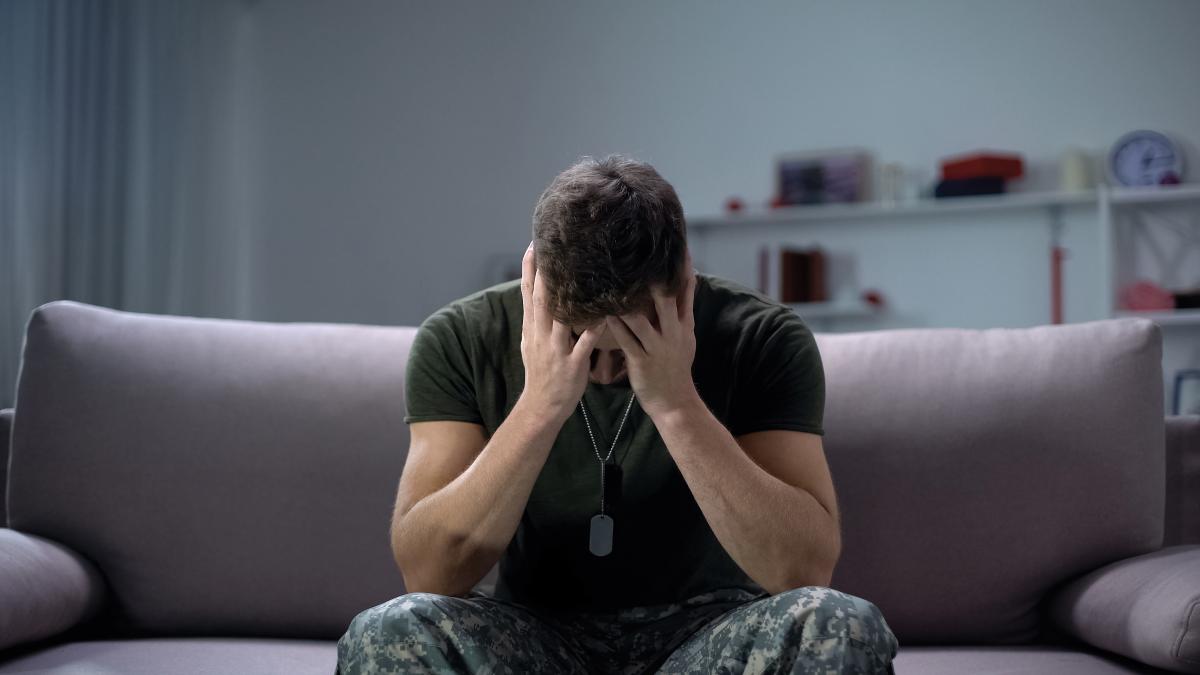 Stock photo of soldier sitting on a couch with his head in his hands