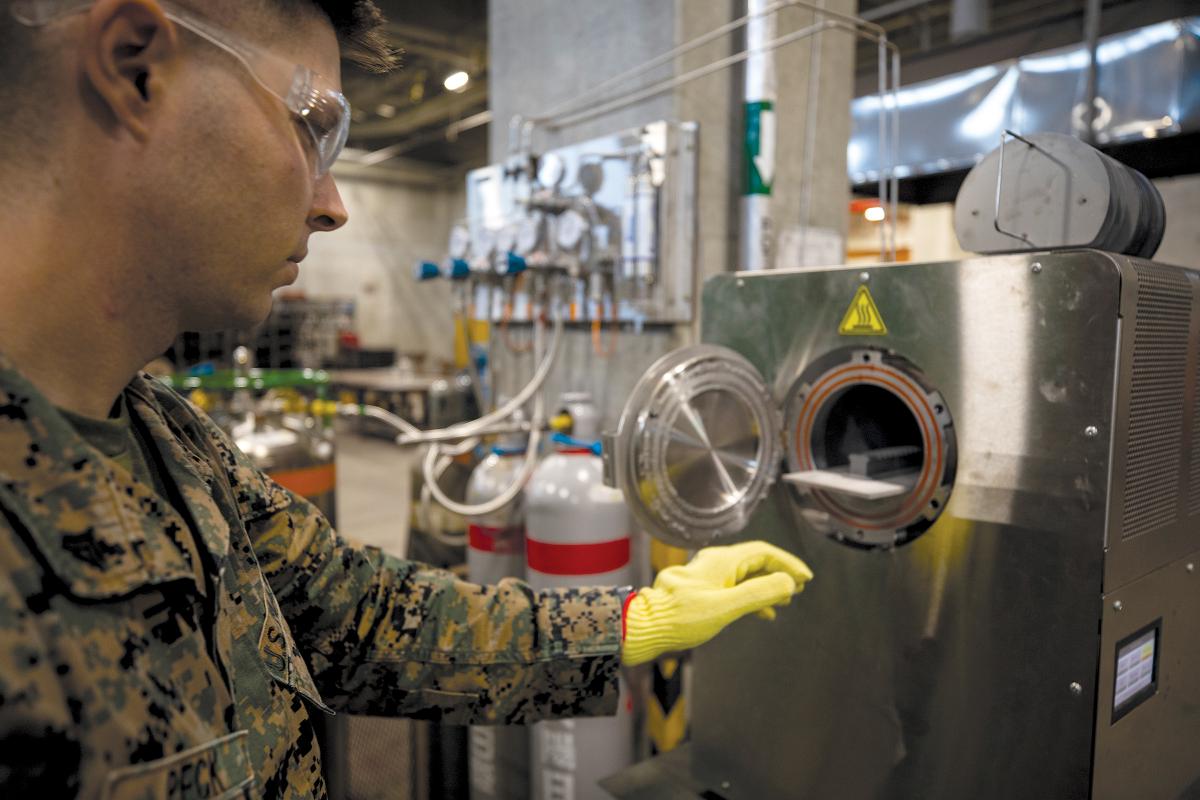 A Marine Corps corporal at Camp Kinser, Okinawa, places a 3-D printed part inside a sinter to bake and fuse. 