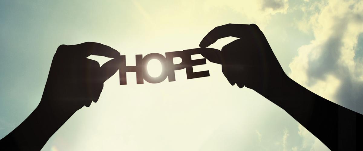 silhouette image of two hands holding a paper cutout of the word "Hope" with sunlight pouring through the letter O
