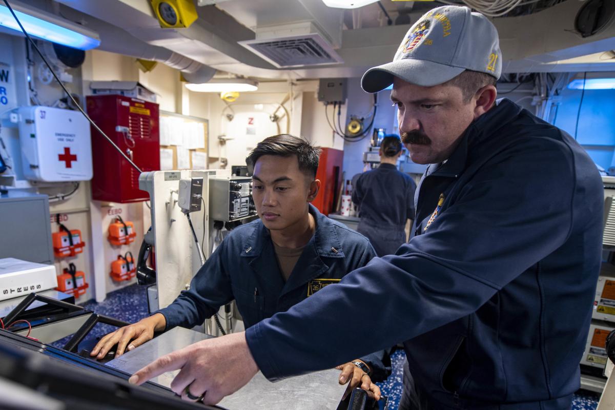 Hull Maintenance Technician First Class Benjamin Cascario, right, trains Lieutenant (junior grade) Jason Punsalan on standing engineering officer of the watch on board the USS John P. Murtha (LPD-26).