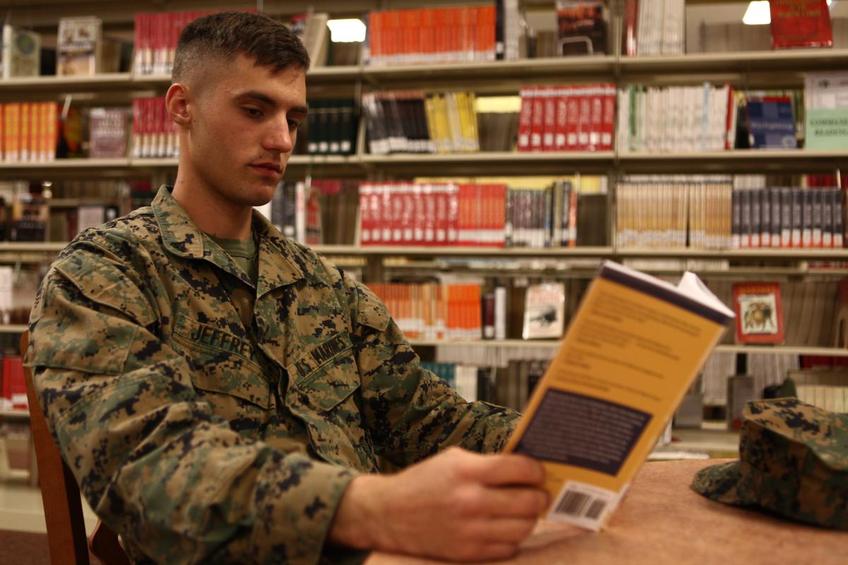 A Marine reading a book in a library.