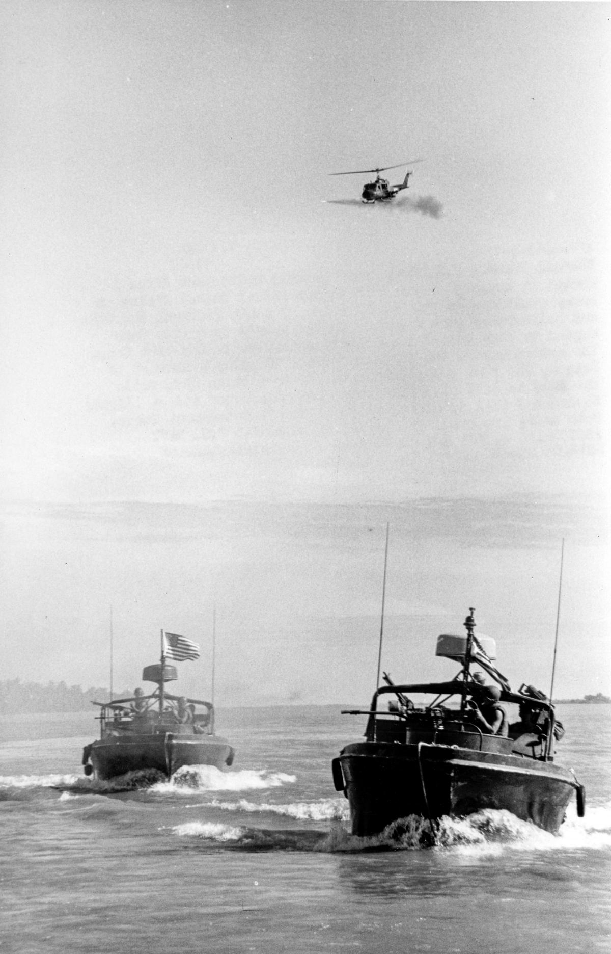U.S. Navy armed gunship helicopter fires a rocket in support of two PBRs (River Patrol Boats)