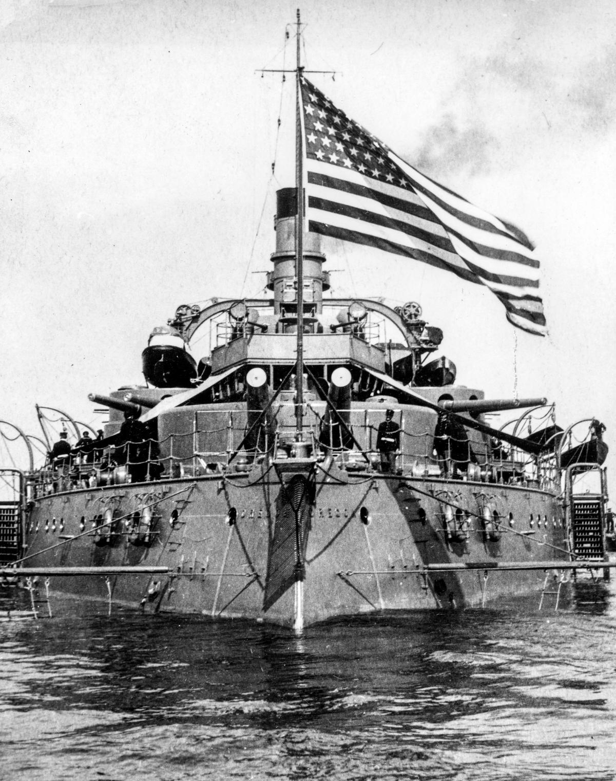 Stern-on view of the battleship Oregon (BB-3) at anchor with boat booms extended