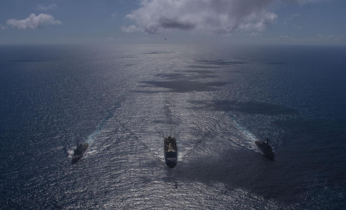 Two U.S. Navy destroyers at sea with a logistics ship in April 2020