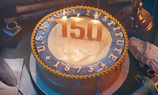 Naval Institute emblem on top of cake with 150th spelled out with lit candles. The cake is sitting on a desk in front of a porthole on a ship. Various items are on the desk including a sword and a quill.
