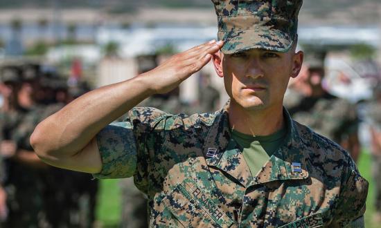 Marine saluting in front of a rifle squad