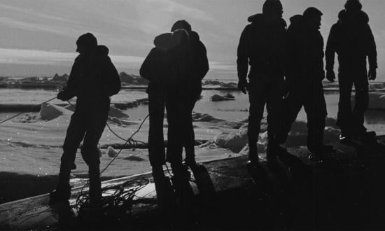 Crewmen of the nuclear-powered attack submarine  USS Queenfish (SSN-651) hold a safety line for scuba divers in a rubber raft near the North Pole. The divers are preparing to observe and photograph the underside of the ice.
