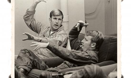 At Naval Air Station Oceana, Virginia, a Navy and Air Force pilot demonstrate a maneuver during a debriefing session after an air combat maneuvering mission. They are participating in a Joint Air Combat Tactics Training Program established to expose each service to the other’s air combat concepts (circa 1972). 
