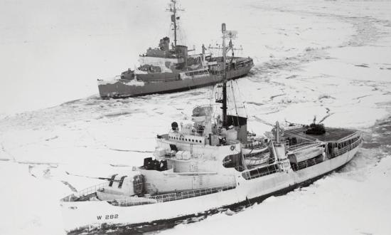 In this solid field of ice in the Bering Sea, two icebreakers try a tandem method of breaking ice. Ramming, backing, and ramming again, the vessels try forcing their way, side-by-side, in a parallel line.