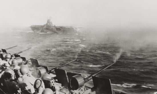Antiaircraft guns firing on board the USS Wasp (CV-18) in December 1944. The USS Yorktown (CV-10) is in the background. Note the Mk 14 gyroscopic reflector sights visible on top of the guns.