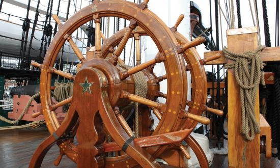 The helm of the USS Constitution shows the characteristic features of ships’ wheels from the time before steam or electric motors controlled the rudder. Two wheels, separated by a winch barrel, allowed extra helmsmen to assist in heavy weather. The barrel is connected through the deck by a series of blocks and tackles to the tiller, which turns the rudder.