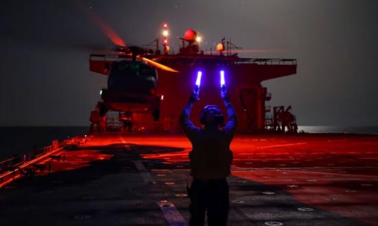 A person guiding a helicopter landing on a ship.