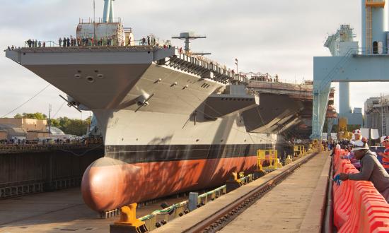 The aircraft carrier John F. Kennedy (CVN-79)—shown in dry dock prior to her christening and 17 December launch—is scheduled to deliver to the Navy in 2022.