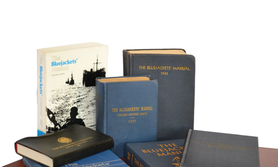 Seven different editions of the Bluejacket's Manual on a table