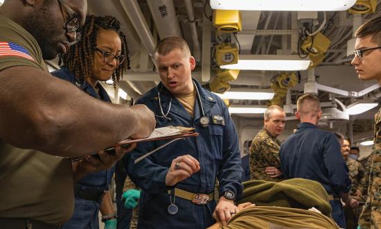 Medical personnel assess a simulated casualty during an exercise on board the USS America (LHA-6) in February 2024. A reader argues that no dilemma exists about going forward or staying in the rear to treat wounded personnel: A lawful order is determinative.