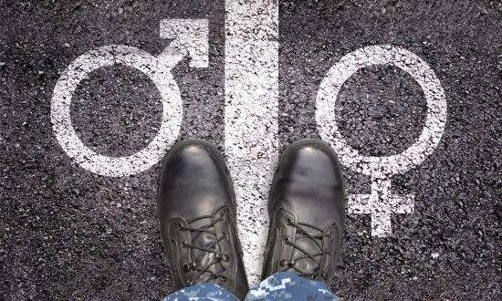 Looking down on legs of a Navy service member standing on a white line on a road with male and female symbols on either side