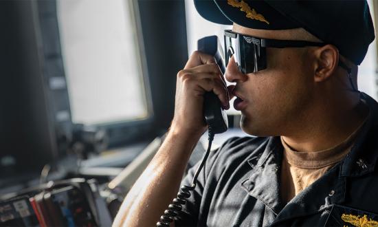 The commanding officer of the Arleigh Burke–class guided-missile destroyer USS Ralph Johnson (DDG-114) communicates with tugboats during a port visit to Guam.