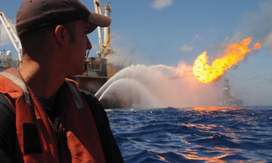 A Coast Guard petty officer looks on from a small boat detached from the USCGC Resolute (WMEC-620)  as oil and gas are flared off at the site of the 2010 Deepwater Horizon oil spill. A post-incident review identified  gaps in the Coast Guard’s marine environmental response preparedness and programs.