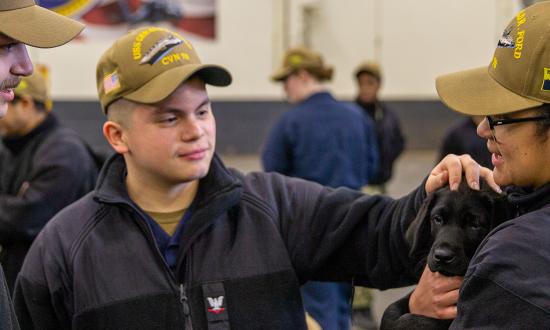 Sailors play with a dog from Mutts with a Mission on board the USS Gerald R. Ford (CVN-76) as part of a morale boosting event. Science has shown dogs can help fight stress—one of many options the Navy should consider.  