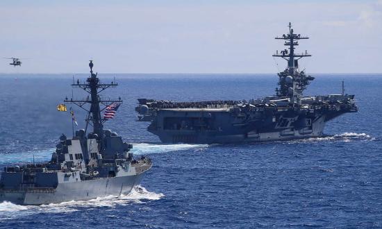 The Arleigh Burke-class guided missile destroyer USS Spruance (DDG 111) sails alongside the Nimitz-class aircraft carrier USS Abraham Lincoln (CVN 72) as an MH-60S Sea Hawk helicopter, assigned to the “Chargers” of Helicopter Sea Combat Squadron (HSC) 14, flies by during an air power demonstration for embarked guests. 