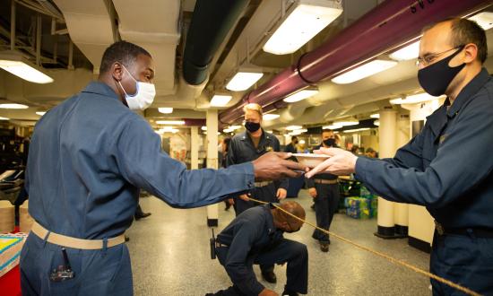 The USS Gerald R. Ford (CVN-78) command master chief hands out cake to sailors to commemorate the ship’s three-year commissioning anniversary. The Ford’s sailors are executing battle messing in spaces that accommodate six-foot social distancing.  