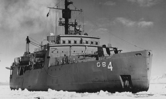 USS Glacier (AGB-4) underway in the channel of McMurdo Sound. The ship's helicopter making an approach to land aboard.