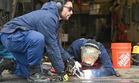 Coast Guardsmen make repairs to the hangar door locking mechanism on board the USCGC Kimball (WMSL-756). The Coast Guard’s motto, Semper Paratus (Always Ready), has been translated culturally into “do more with less,” which can be disheartening for members.
