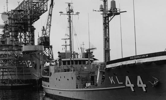 Starboard bow view of USS Pueblo (AKL-44) lying at a pier before it was redesignated as USS Pueblo (AGER-2). The 1968 incident highlights the danger of maintaining geographically dispersed defense commitments.