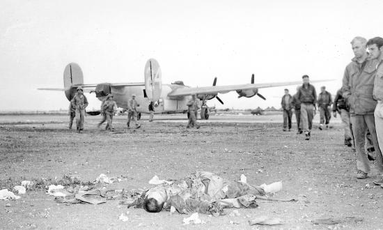 Marines at Okinawa’s Yontan Airfield gaze at the body of a Japanese commando while a B-24 stands in the background