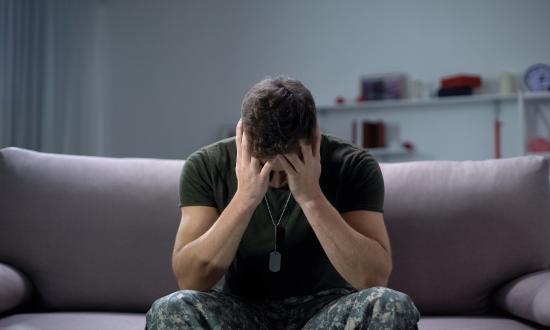 Stock photo of soldier sitting on a couch with his head in his hands