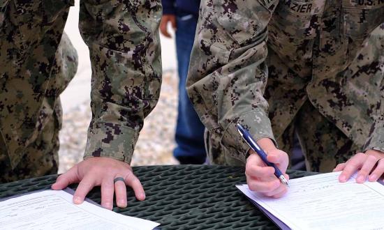 A dual-military couple signs their reenlistment papers together. Creating new policies that allow for more career flexibility for all officers is crucial to making it possible for more women to stay in the Navy longer