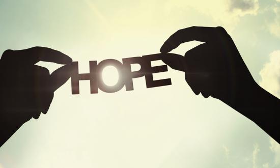 silhouette image of two hands holding a paper cutout of the word "Hope" with sunlight pouring through the letter O