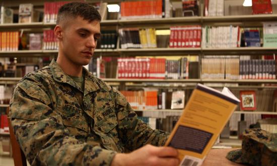 A Marine reading a book in a library.