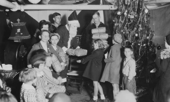 A seagoing Santa Claus distributes presents to children aboard the USS Antares (AG-10) on Christmas day, 1931.