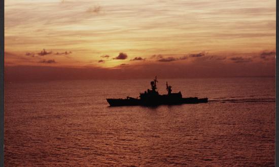 A port side silhouette of the USS Sterett (CG-31) underway at dawn.