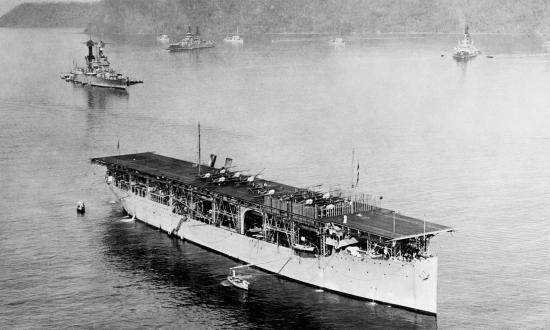 USS LANGLEY (CV-1) With Bought VE-7 aircraft on deck. In the background are four 4-stack destroyers and a TENNESSEE class battleship on the left and two New Mexico class battleships (center and right). Circa 1923.