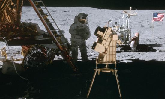Astronaut John Young in shadow of Lunar Module behind ultraviolet camera