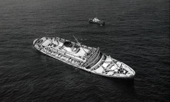 The liner Andrea Doria heels over to starboard as a Coast Guard cutter stands by