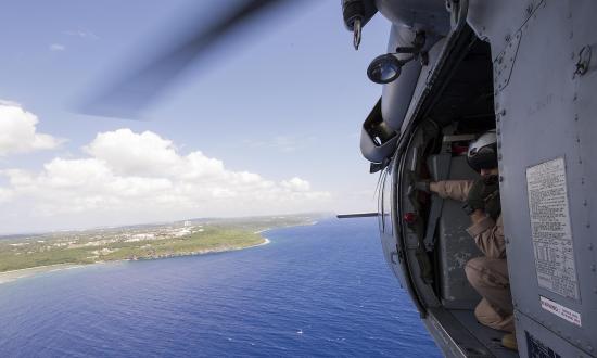 A Navy air crewman scans horizon from helicopter door