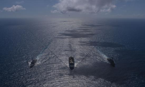 Two U.S. Navy destroyers at sea with a logistics ship in April 2020